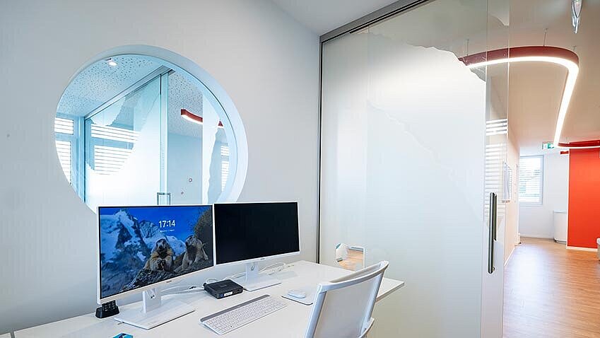 Computerarbeitsplatz vor Bullauge (rundes Fenster) in einen anderen RAum