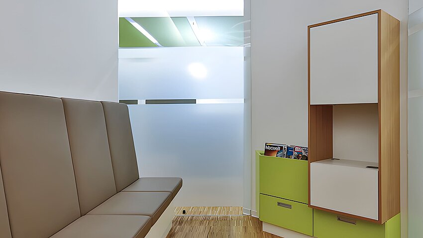 Wartebereich mit grauer Sitzbank grüner Ablage und satiniertem Glas