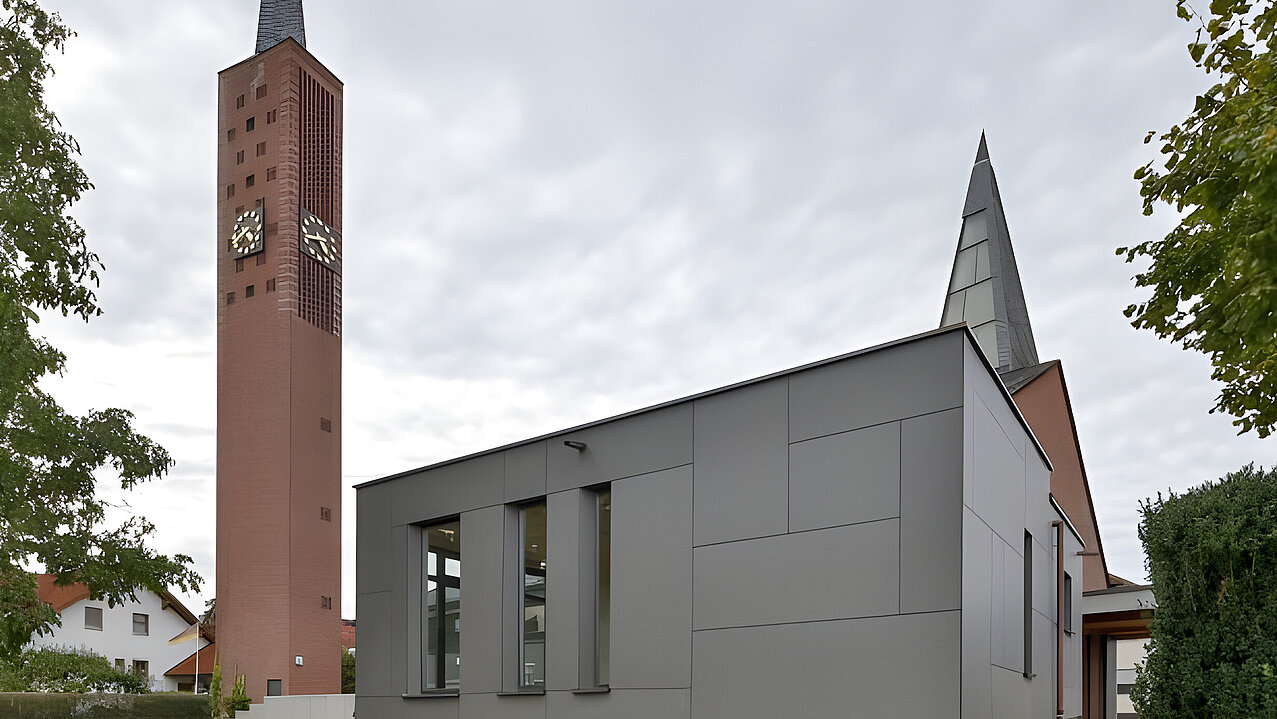 Kirchturm mit Uhr neben modernem grauen Anbau