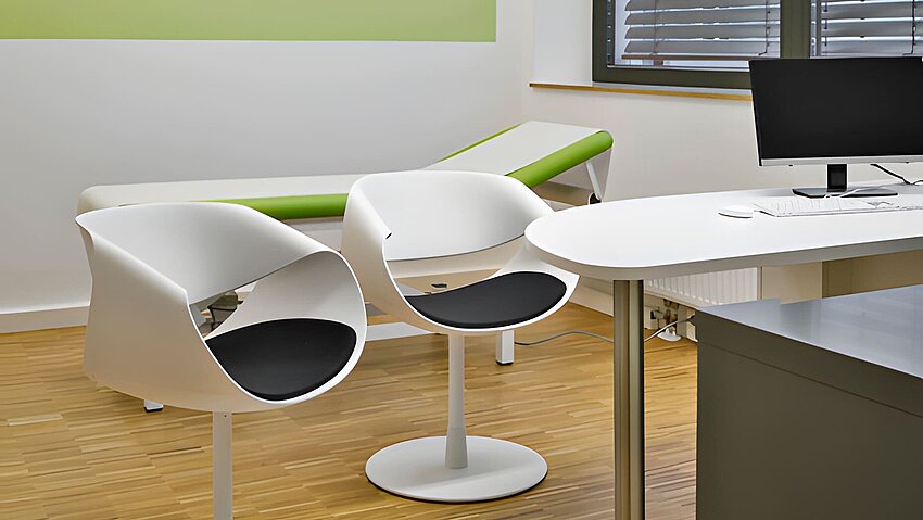 Klares Untersuchungszimmer mit weißen Drehsesseln und grüner Liege