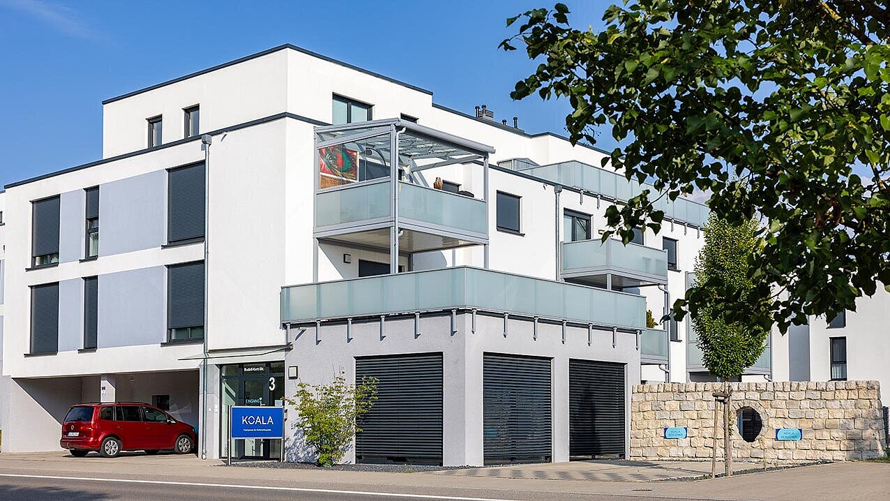 Außenansicht des weißen Gebäudes im Bauhausstil, rotes Auto auf Kundenparkplatz