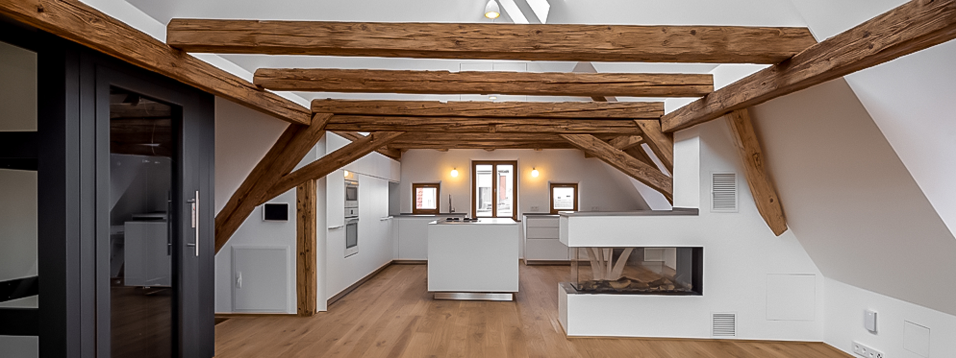 Ausgebautes Dachgeschoss mit sichtbaren Holzbalken, offener Küche und Kamin